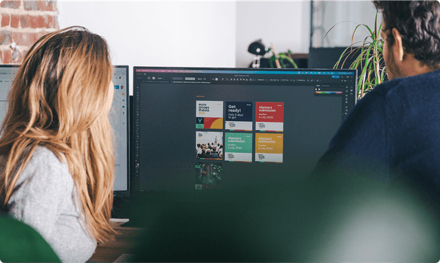 Brand collateral Two people working at a desk, viewing design software on a large monitor displaying colorful graphics and text.
