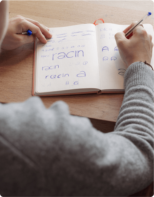 Stylescape Person practicing handwriting in a notebook with various styles of the word "racin" using a blue pen.