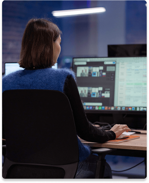 Brand book Person with short hair working on a computer with multiple screens displaying various data and images in a dimly lit office.