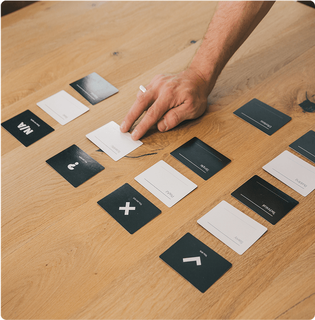 Kick-off workshop(s) A hand arranging black and white cards with symbols and words on a wooden table.