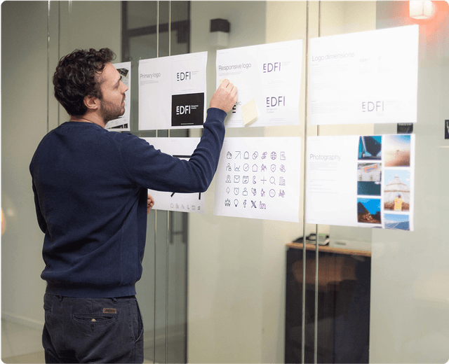 Brand book Man reviewing design documents on a glass wall, featuring logos, icons, and photography samples.