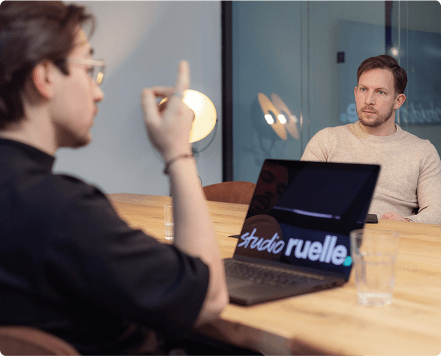 Kick-off workshop(s) Two people in a meeting, one gesturing while the other listens. A laptop with "studio ruelle" on the screen is on the table.