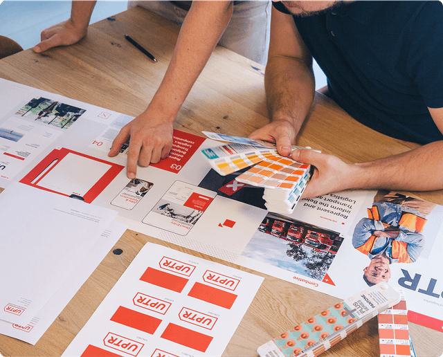 Brand identity design People reviewing design materials and color swatches on a wooden table, focusing on branding and layout options.